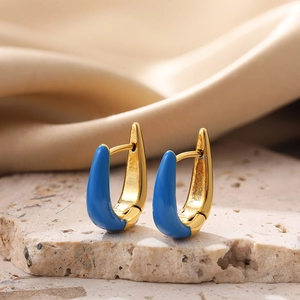 Detailed close-up of U-shaped gold earrings with blue enamel finish on textured stone