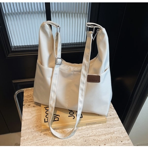 Close-up of white canvas hobo bag with brown leather brand tag on marble surface