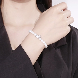 Detail of shell pearl bracelet with cute gold pig charm worn on a female wrist