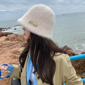 Detailed close-up of plush bear ear bucket hat in beige faux fur with metal logo tag