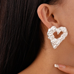 Close-up of oversized silver heart earrings with a textured liquid metal finish