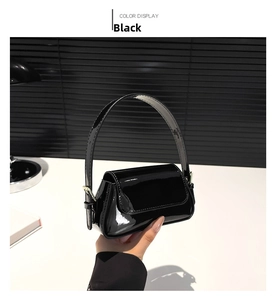 Close-up of a glossy black patent leather baguette mini bag with gold metallic buckle detail
