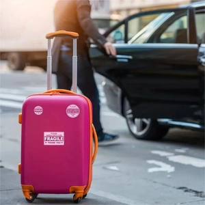Close-up of bright pink luggage with orange details and fragile warning stickers on it