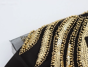 Close-up of golden sequins and beadwork on the black mesh shoulder of a blazer dress