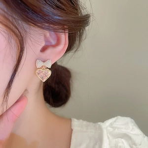 Close-up of pink heart gemstone earrings with pearl bow and gold-plated details on ear