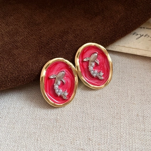 Vue macro des boucles d'oreilles ovales en émail rouge avec bords dorés et poissons argentés