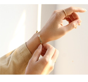 Detailed shot of gold open bangle featuring two round white zircons on a model wrist