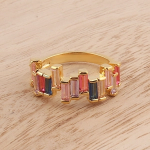 Golden ring with slanted rainbow crystals and colorful gemstones on wood background