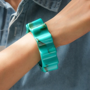 Primo piano di un bracciale rigido in acrilico marmorizzato verde su sfondo di jeans