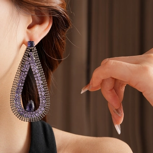 Close-up of teardrop earring featuring purple rhinestones on a dark filigree base
