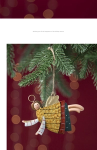 Close-up of painted metal Christmas angel ornament hanging on green pine branches