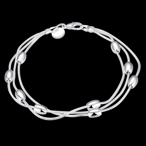 Detail of silver-plated multi-layer bracelet with polished oval metallic beads on dark background
