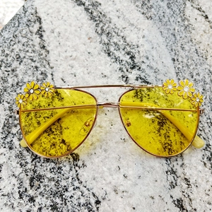 Close-up of yellow lens sunglasses with golden frame and daisy flower details