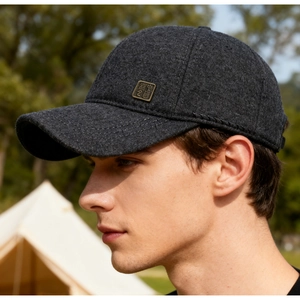Close-up of a dark grey wool baseball cap with a vintage metal logo detail on the side