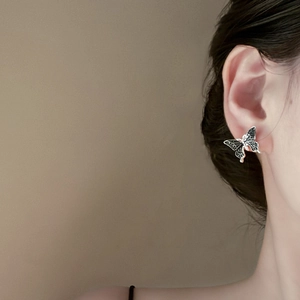Detailed close-up of a silver-tone butterfly earring with black delicate wing textures