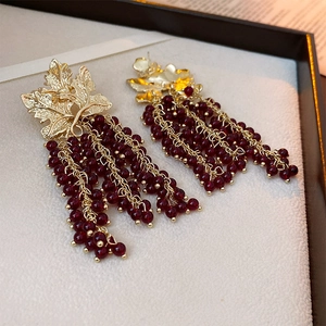 Detail of vintage gold leaf earrings with long dark red berry tassel beads on a display tray