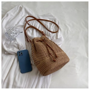 Detail of khaki straw bucket bag with brown leather drawstring and thin shoulder strap