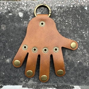 Detail view of brown palm-shaped leather keychain with bronze metal spring clasp and studs