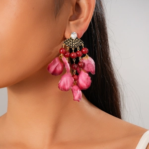 Model wearing a fan-shaped earring with red beads and fabric petals on a grey background