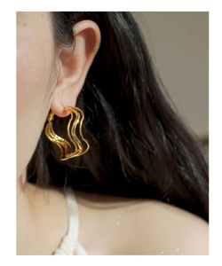 Close-up of a gold irregular wavy hoop earring worn by a model for a chic modern look