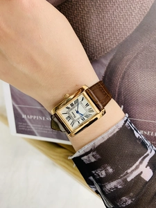 Detail of a rectangular gold watch with Roman numerals and brown leather strap on wrist