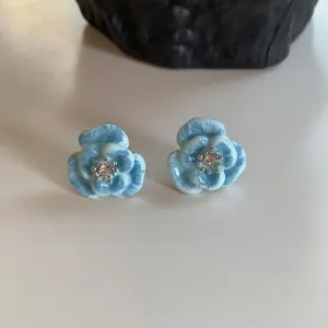 Macro detail of light blue camellia earrings with sparkling central zirconia inlays