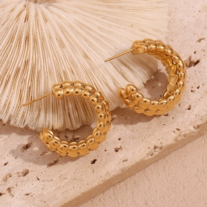Macro shot of gold-plated stainless steel woven C-hoop earrings on white coral