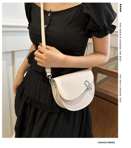 Close-up of a white saddle bag with silver buckle worn by a model in fashion outfit