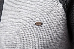 Close-up of light gray knit fabric texture and brand logo detail on half-zip sweater