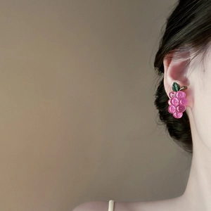Close-up of a pink grape-shaped resin earring worn on a model with green leaf detail
