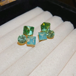 Macro shot of geometric flower earrings with green and blue gemstones in gold setting