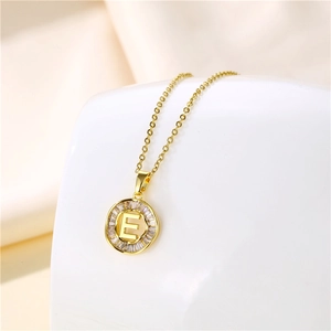 Detail of 18K gold letter E pendant with cubic zirconia inlay on a beige textile base