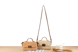 Close-up of woven straw crossbody bags in brown and cream with metal buckles