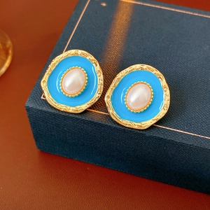 Macro detail of vintage gold pearl earrings with blue enamel and textured metal surface