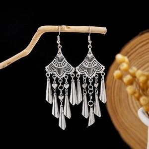 Close-up of bohemian silver tassel earrings with heart accents on a rustic branch