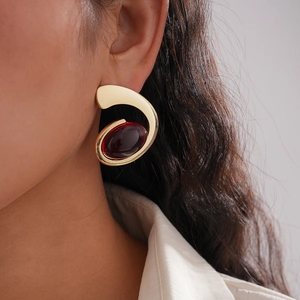 Irregular oval gold metal earrings with deep red resin stone on a female model