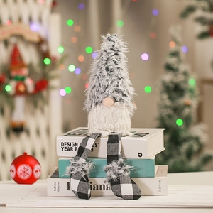 Plush Christmas gnome ornament with long legs sitting on books by a warm holiday tree