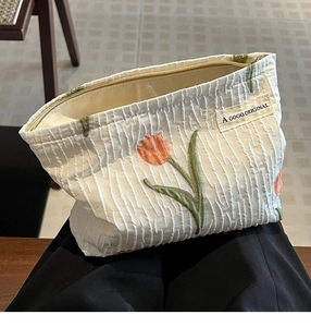 Close-up of white canvas makeup bag with tulip embroidery and gold zipper detail