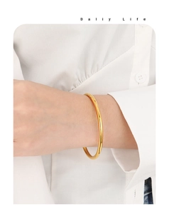 Close-up of minimalist 4mm solid gold finish bangle worn on a female wrist over white shirt