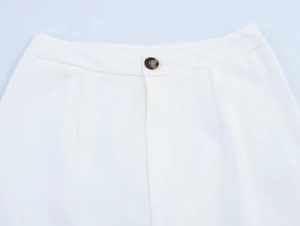 Detail of white trousers featuring a wide waistband and classic tortoiseshell button
