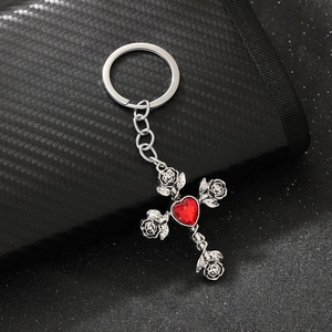 Macro detail of gothic silver cross keychain with red heart gem and carved roses