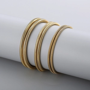 Three gold plated stainless steel snake bone necklaces layered on a grey cylinder display