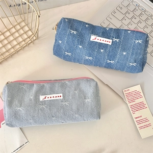 Close-up of denim bow pencil cases with pink zippers and woven SOZAKKA labels on desk