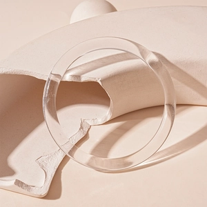 Artistic close-up of a minimalist clear acrylic round bangle on geometric blocks