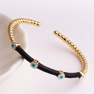 Detailed macro view of gold plated bamboo bangle with blue evil eye charms on white ceramic