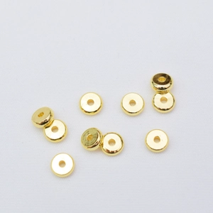 Close-up of flat gold-plated spacer beads for DIY jewelry making on white fabric