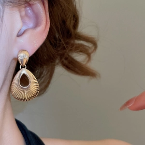 Close-up of golden teardrop pendant earrings with textured radial pattern on a model
