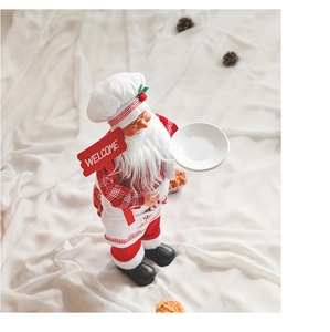 Close-up of Santa chef doll with Welcome sign and tray on white fabric background