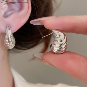 Close-up of silver shell-shaped stud earrings with polished ripple texture and metallic glow