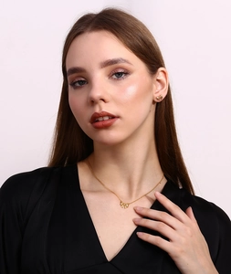 Close-up of model wearing gold ribbon bow pendant necklace and matching stud earrings